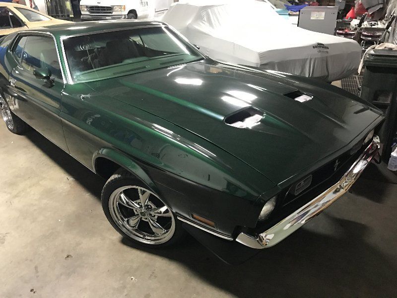 A green mustang is parked in a garage next to other cars.