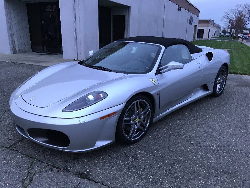 A silver ferrari f430 convertible is parked in front of a building.