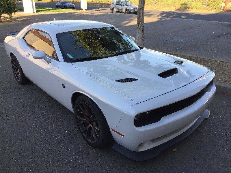 A white dodge challenger is parked on the side of the road with new tinted windows and clear bra