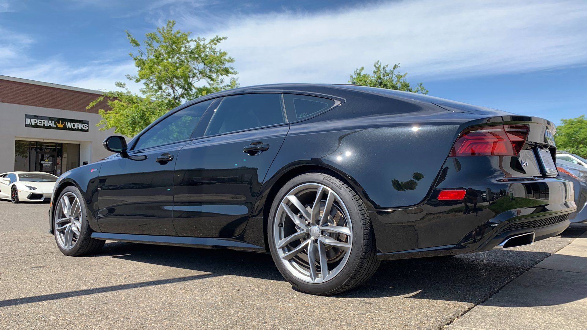 A black audi a7 is parked on the side of the road in front of a building.