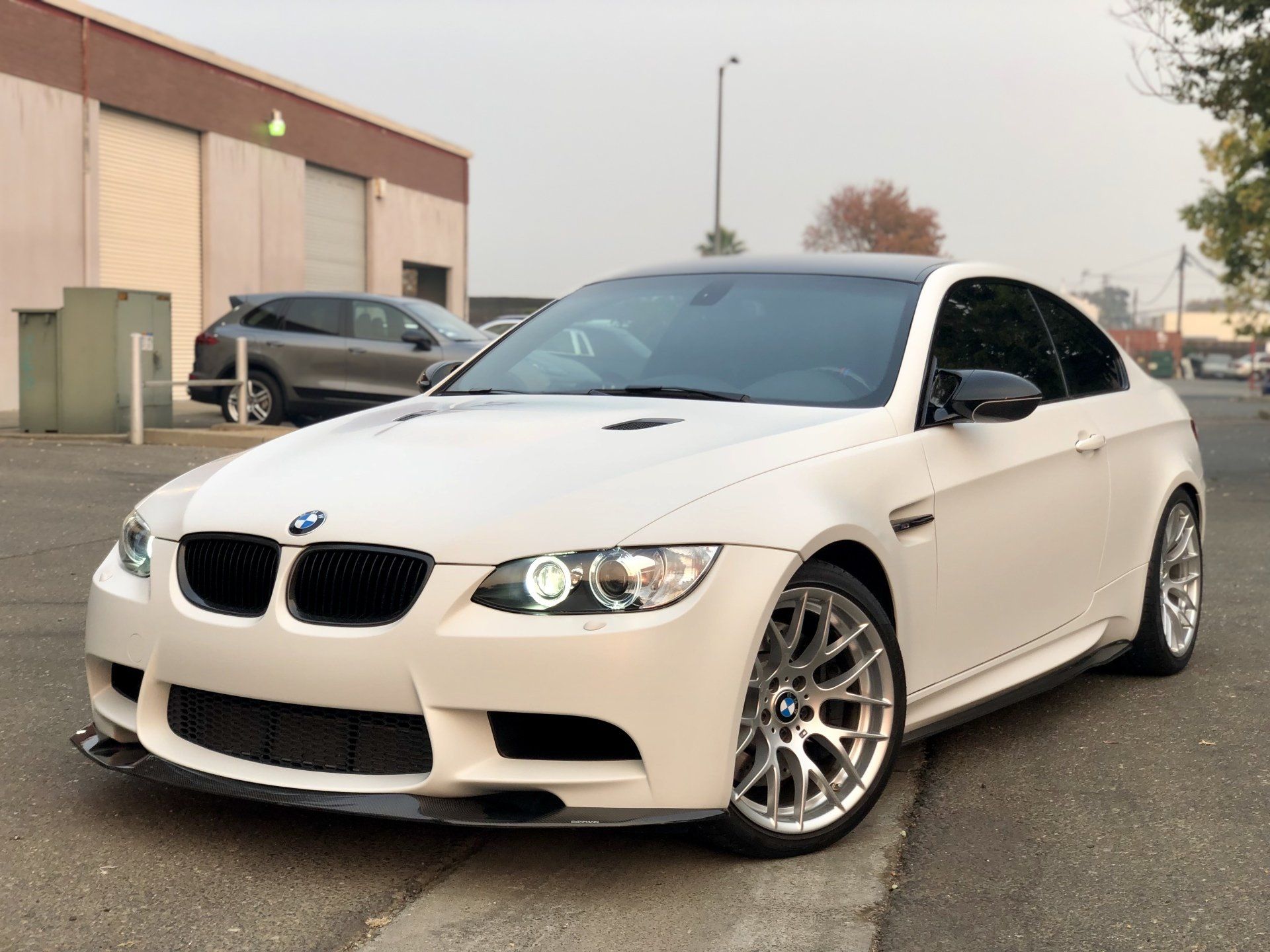 A white bmw m3 is parked on the side of the road in front of a building.