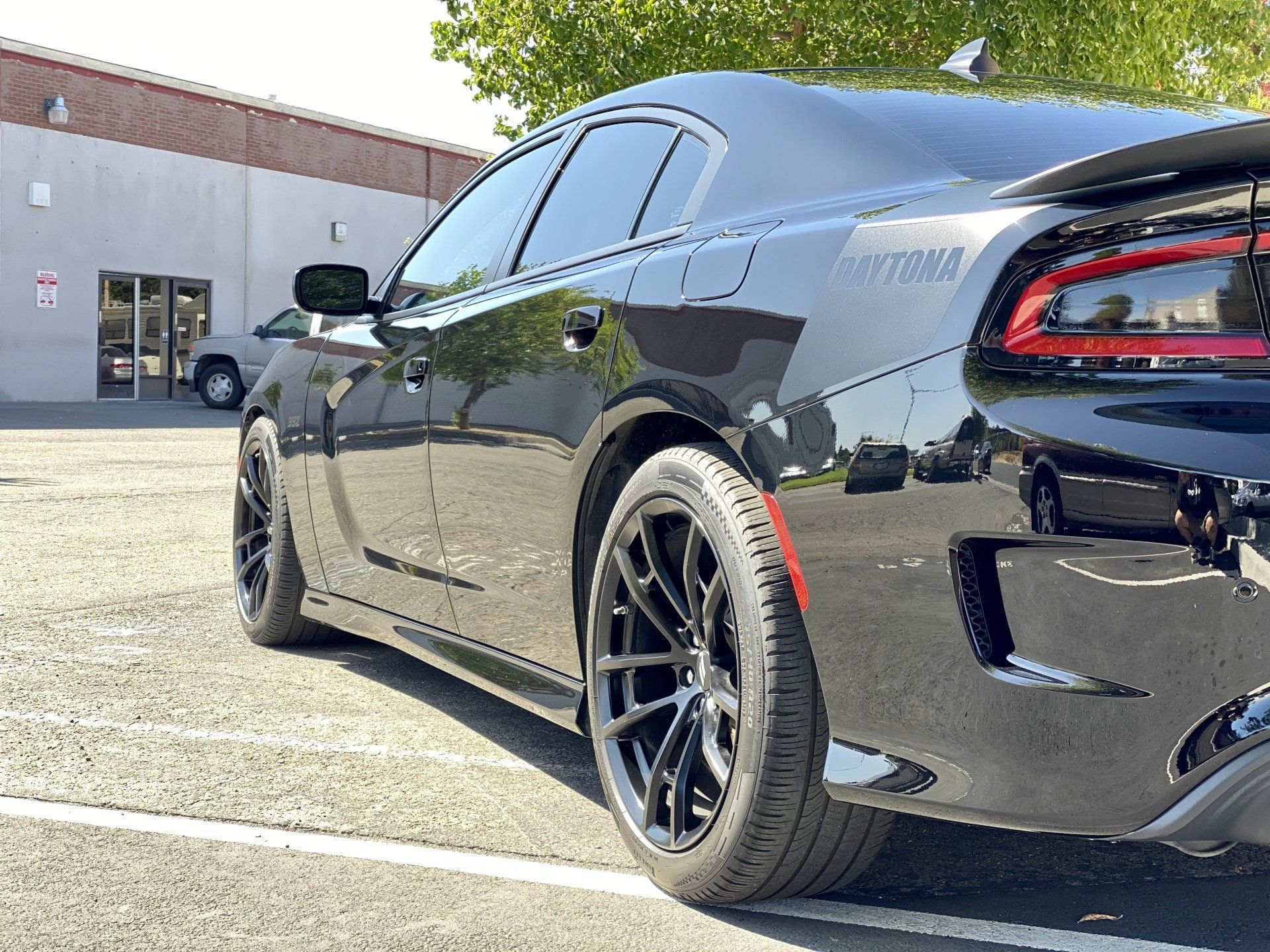 A black dodge charger is parked in a parking lot in front of a building.