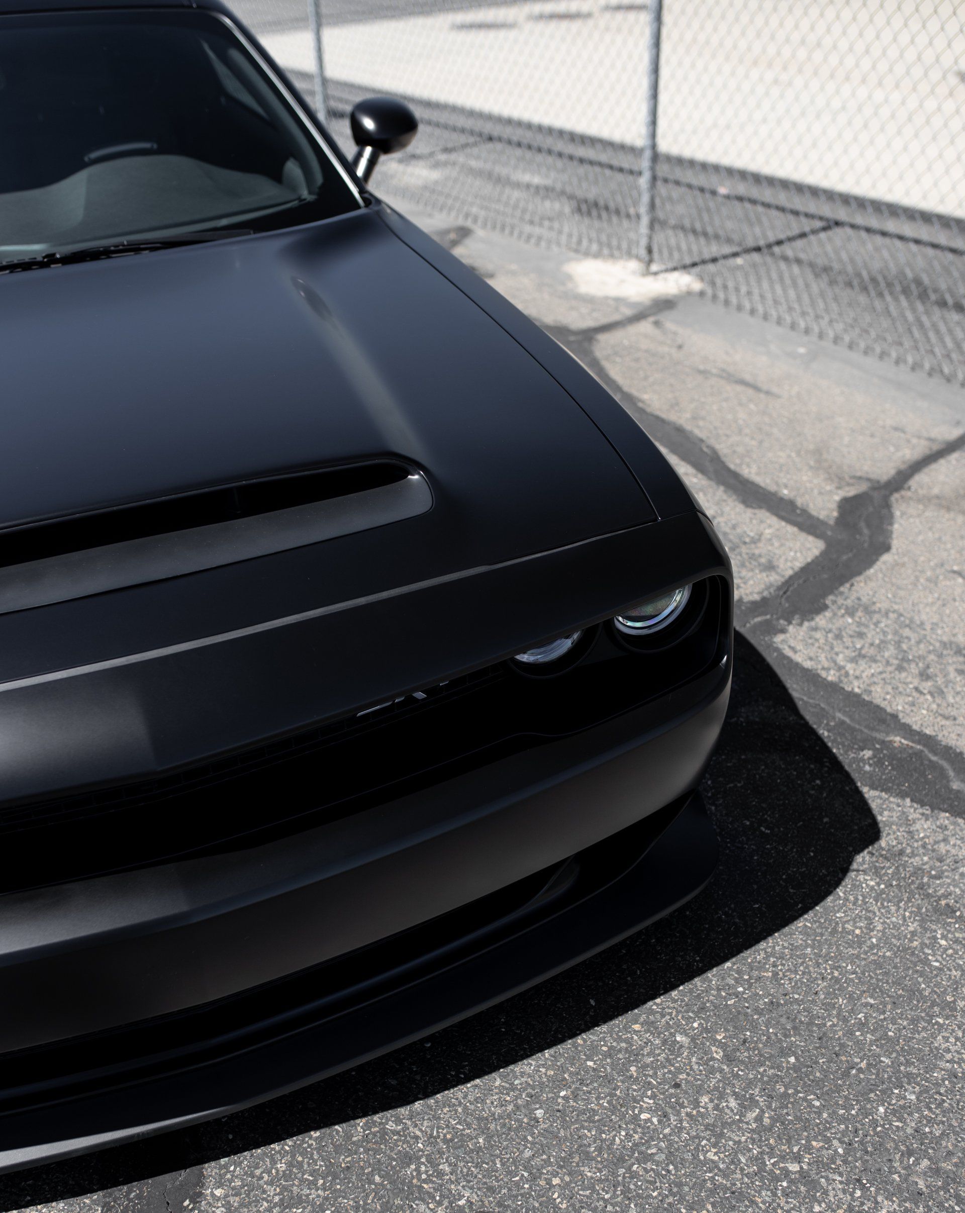 A black car is parked in front of a chain link fence