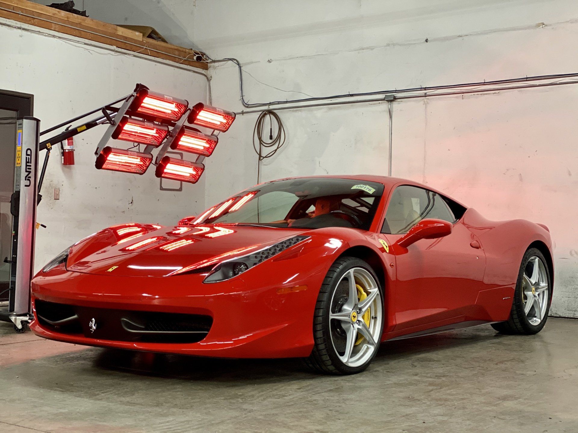 A red ferrari is parked in a garage under a row of lights.