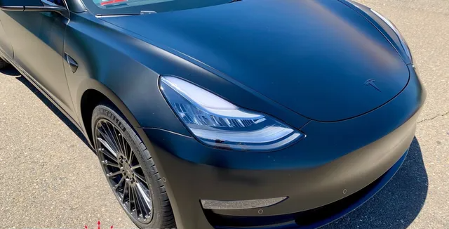 A black tesla model 3 is parked on the side of the road.