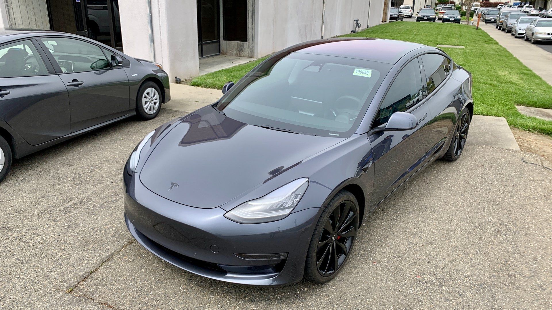A tesla model 3 is parked in a driveway next to a building.