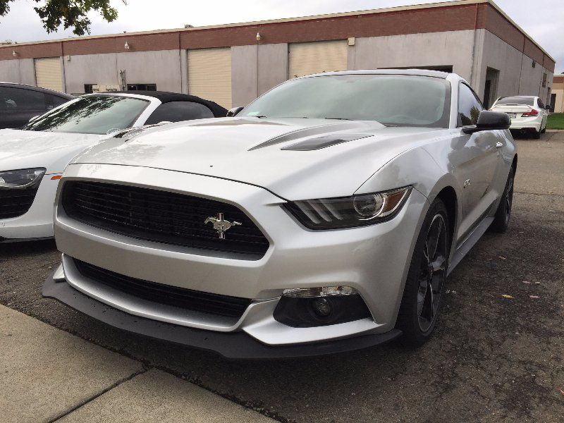 A silver mustang is parked in front of a building.
