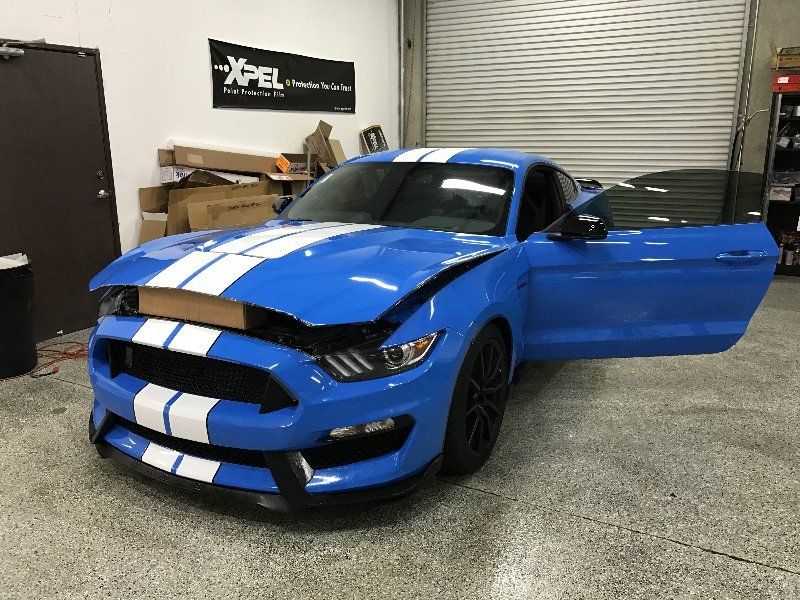 A blue mustang with white stripes is parked in a garage with its doors open.