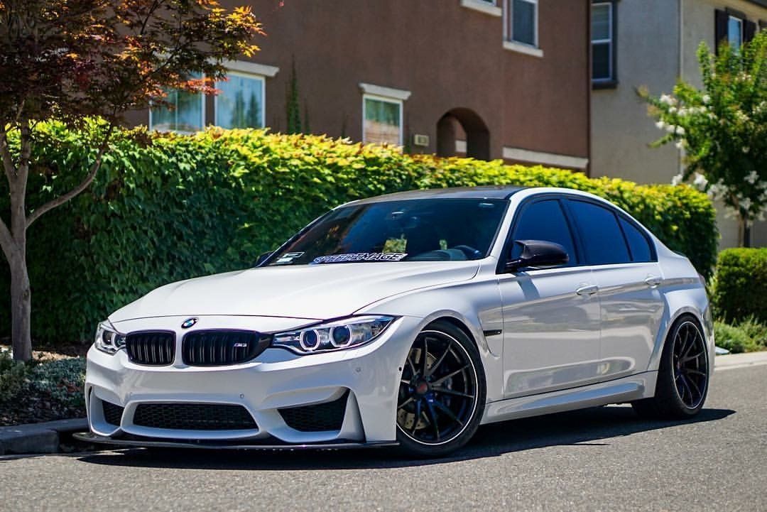 A white bmw m3 is parked on the side of the road in front of a house.