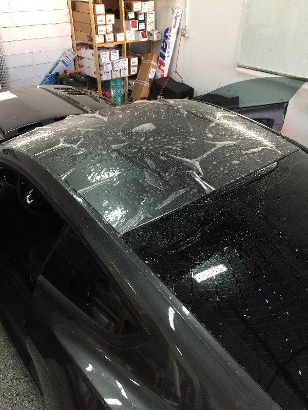 A black car is parked in a garage with the roof covered in water.