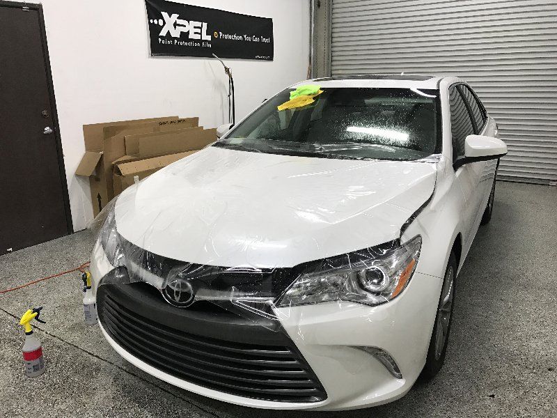 A white toyota camry is wrapped in plastic in a garage.