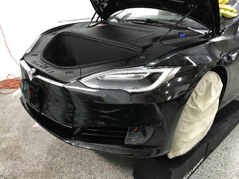 A black tesla model s with the hood open is sitting on a ramp in a garage.