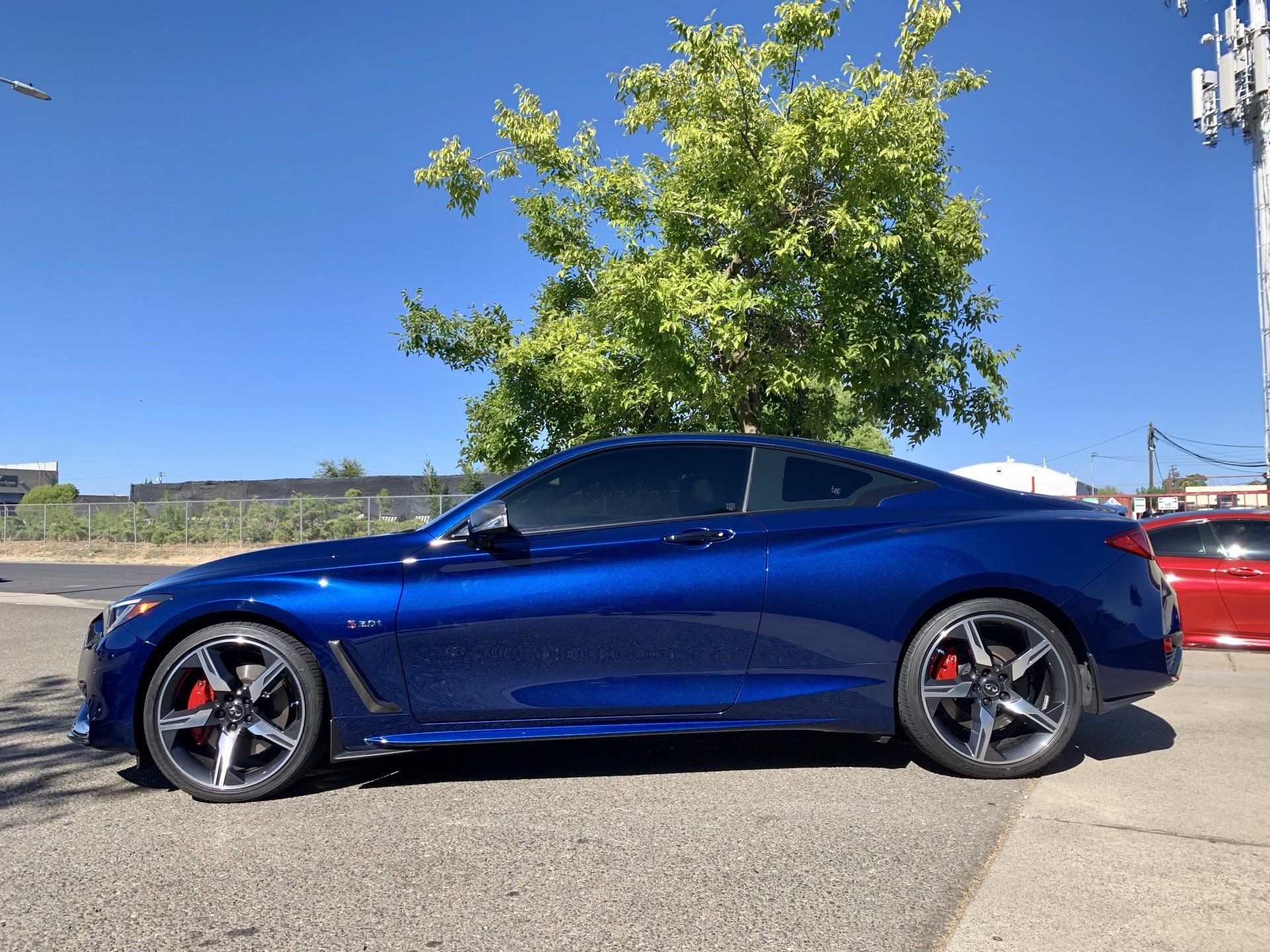 A blue car is parked on the side of the road next to a tree.
