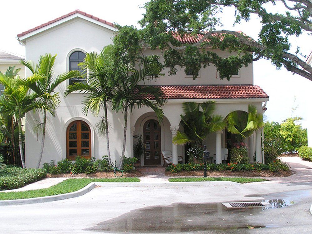 a white house with a red tile roof is surrounded by palm trees