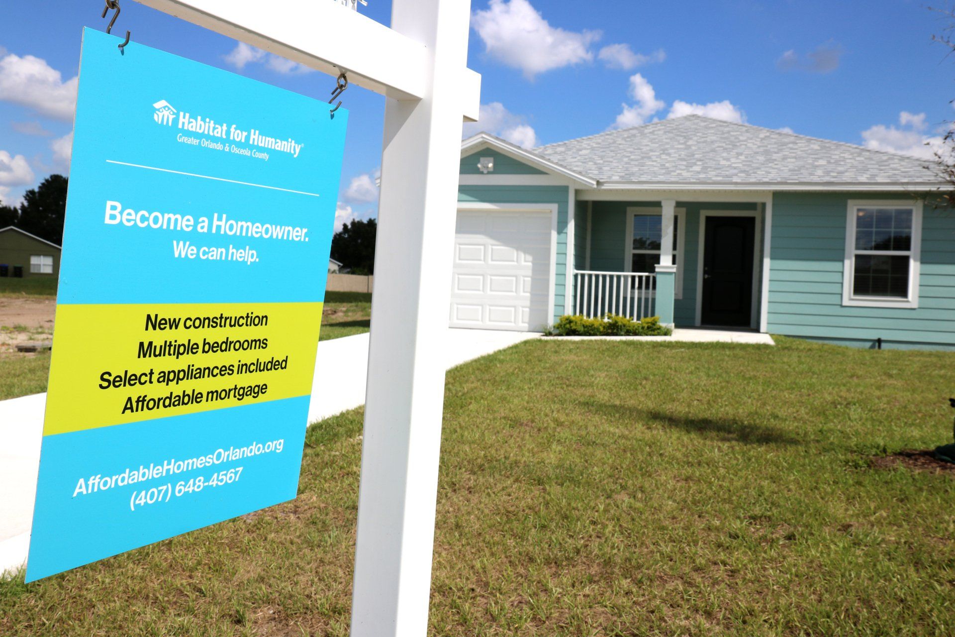 A For Sale sign sits in front of a blue house.