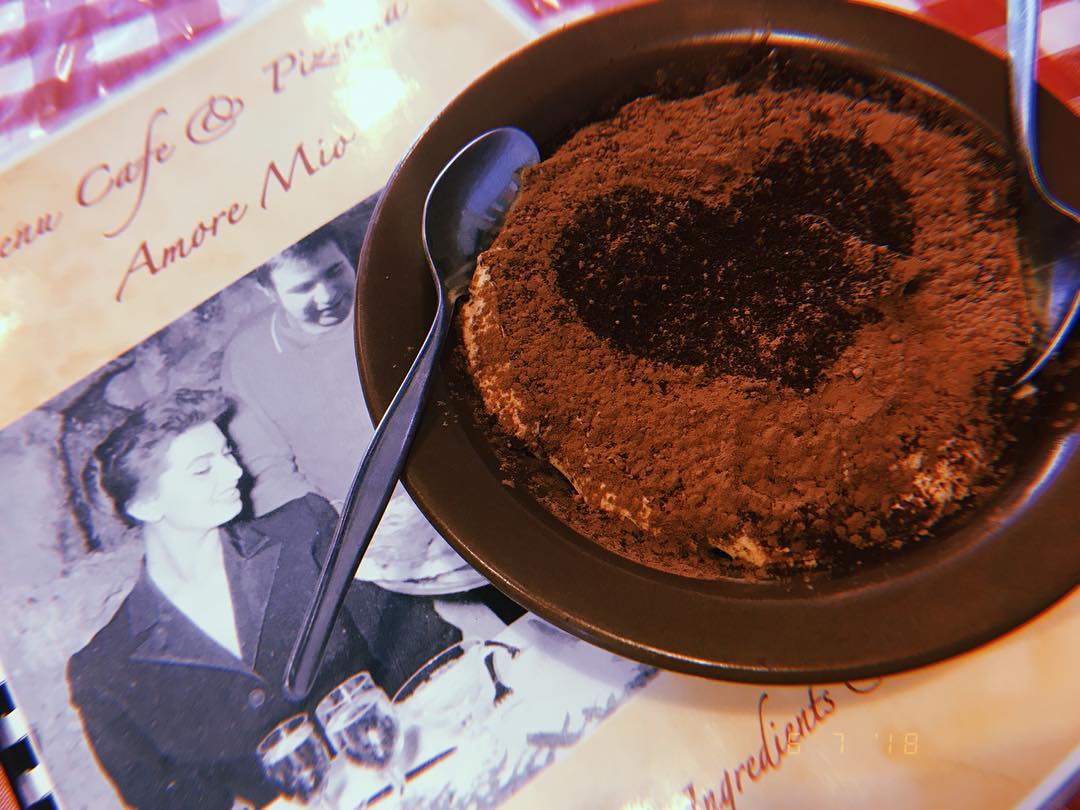 Tiramisu dessert on a brown plate dusted with cocoa, with a heart design, on a cafe menu.