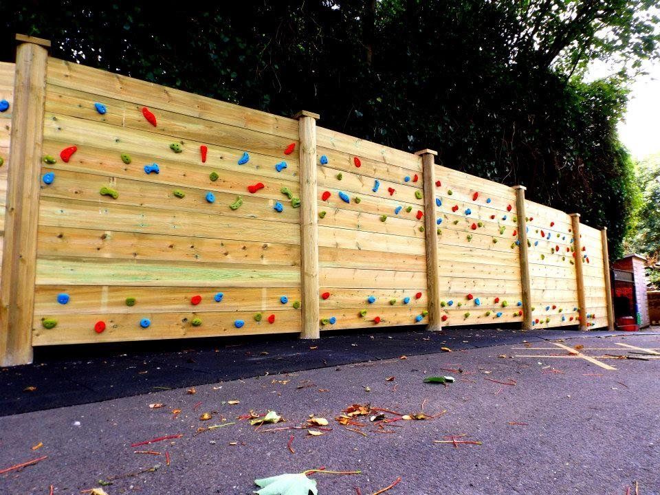 Wooden climbing wall with colorful holds outside, against a tree backdrop.