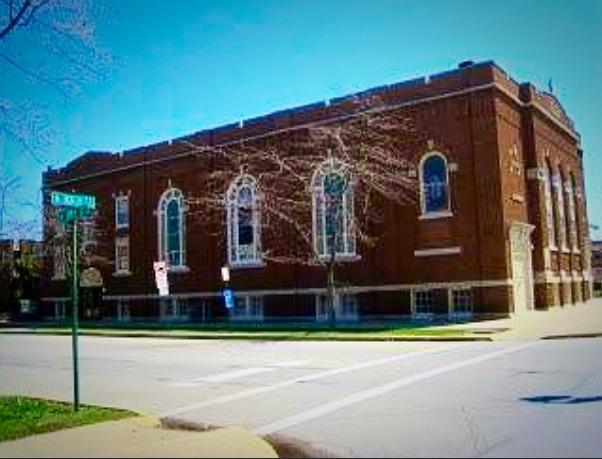 A large brick building with a lot of windows is on the corner of a street.
