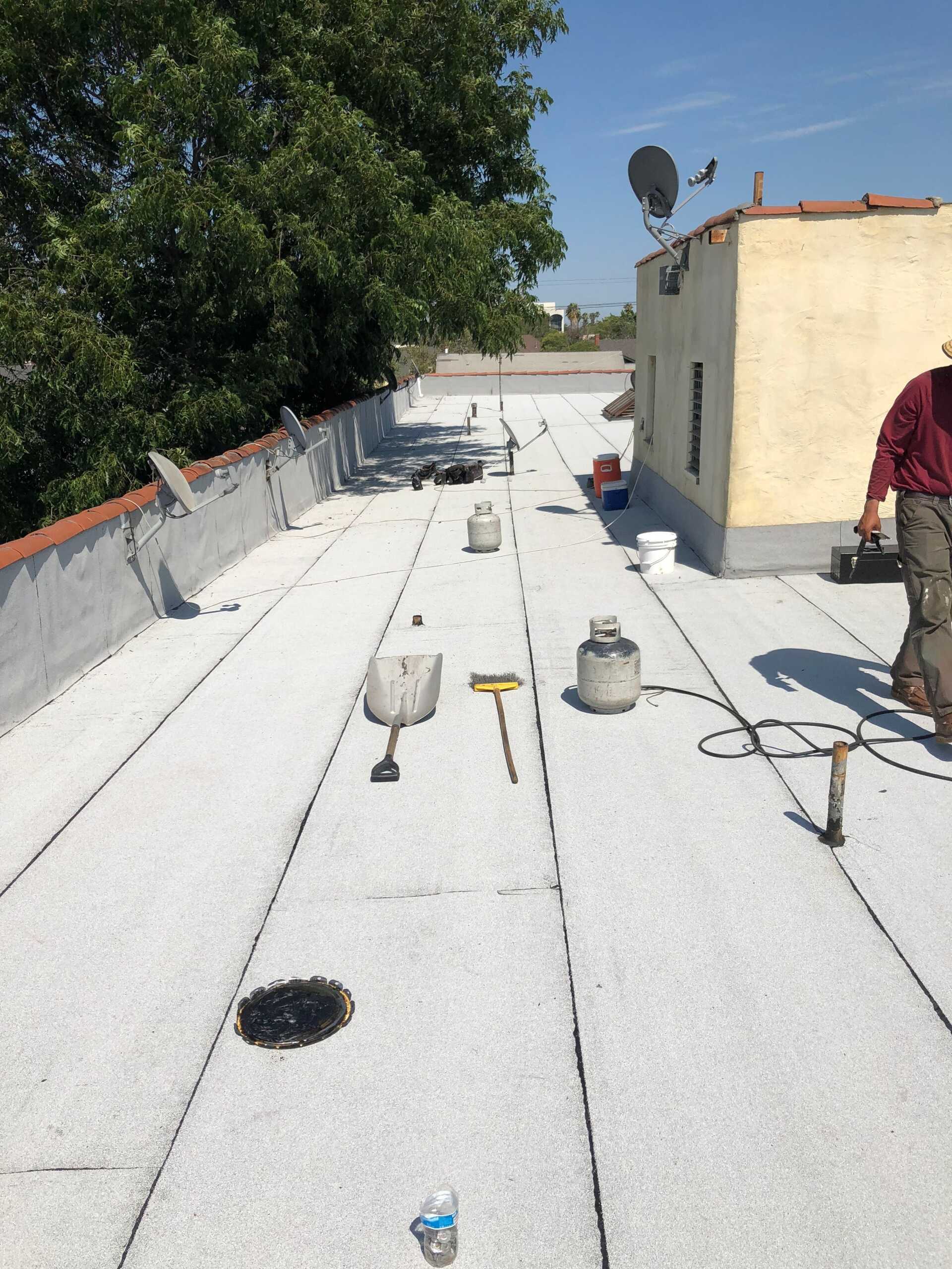 Rooftop under construction with white waterproofing, tools, and a person working near the right edge