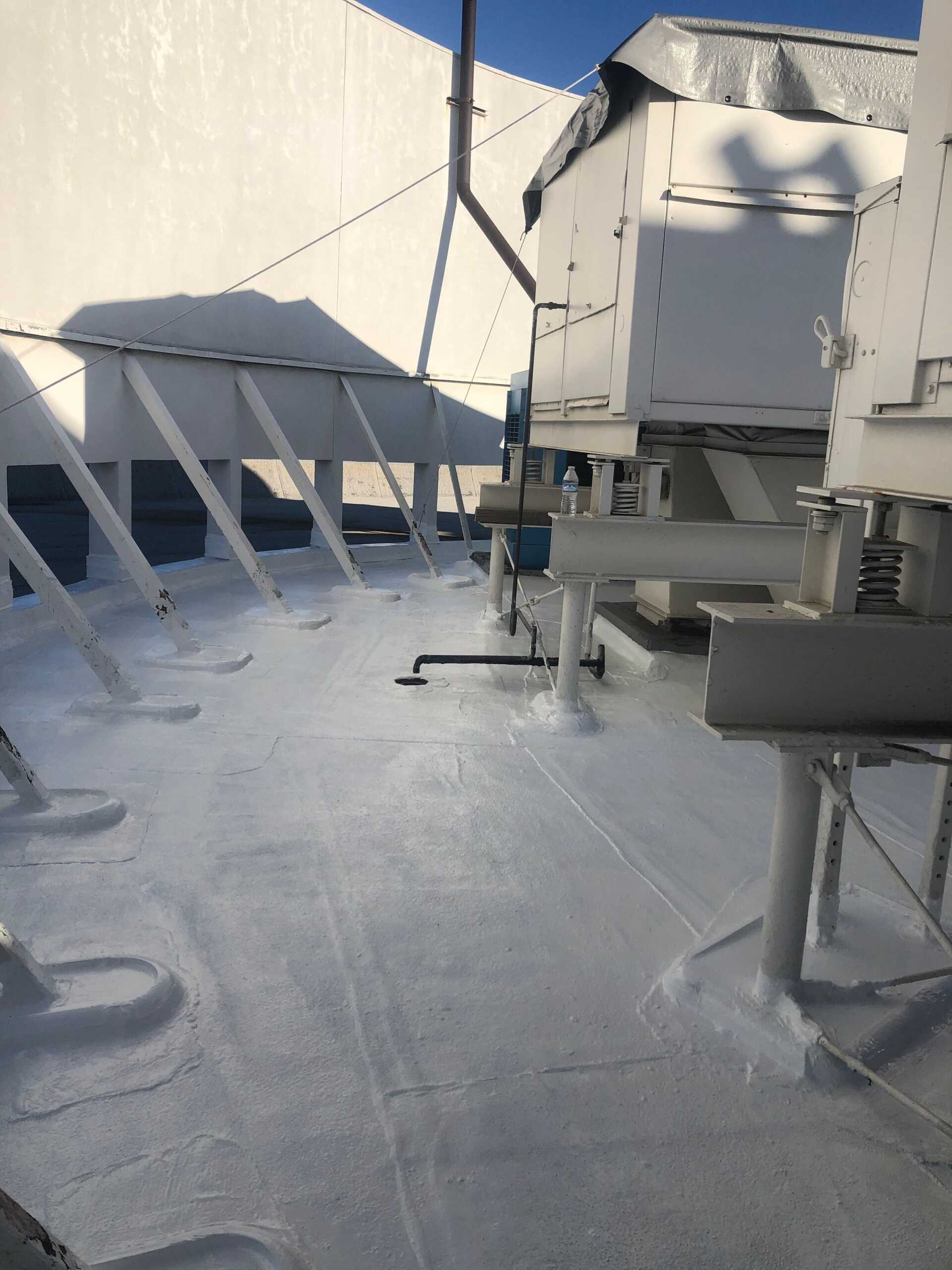 Snow-covered rooftop with HVAC units, pipes, and a clear sky shadowed by railing.