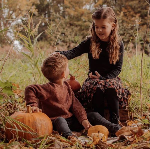 Twee kinderen in een herfstomgeving: een meisje aait een jongen over zijn hoofd, pompoenen in de buurt.