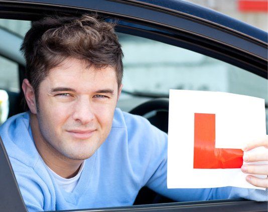 Happy teenage boy showing holding a modern car key and a learner plate while sitting behind the wheel