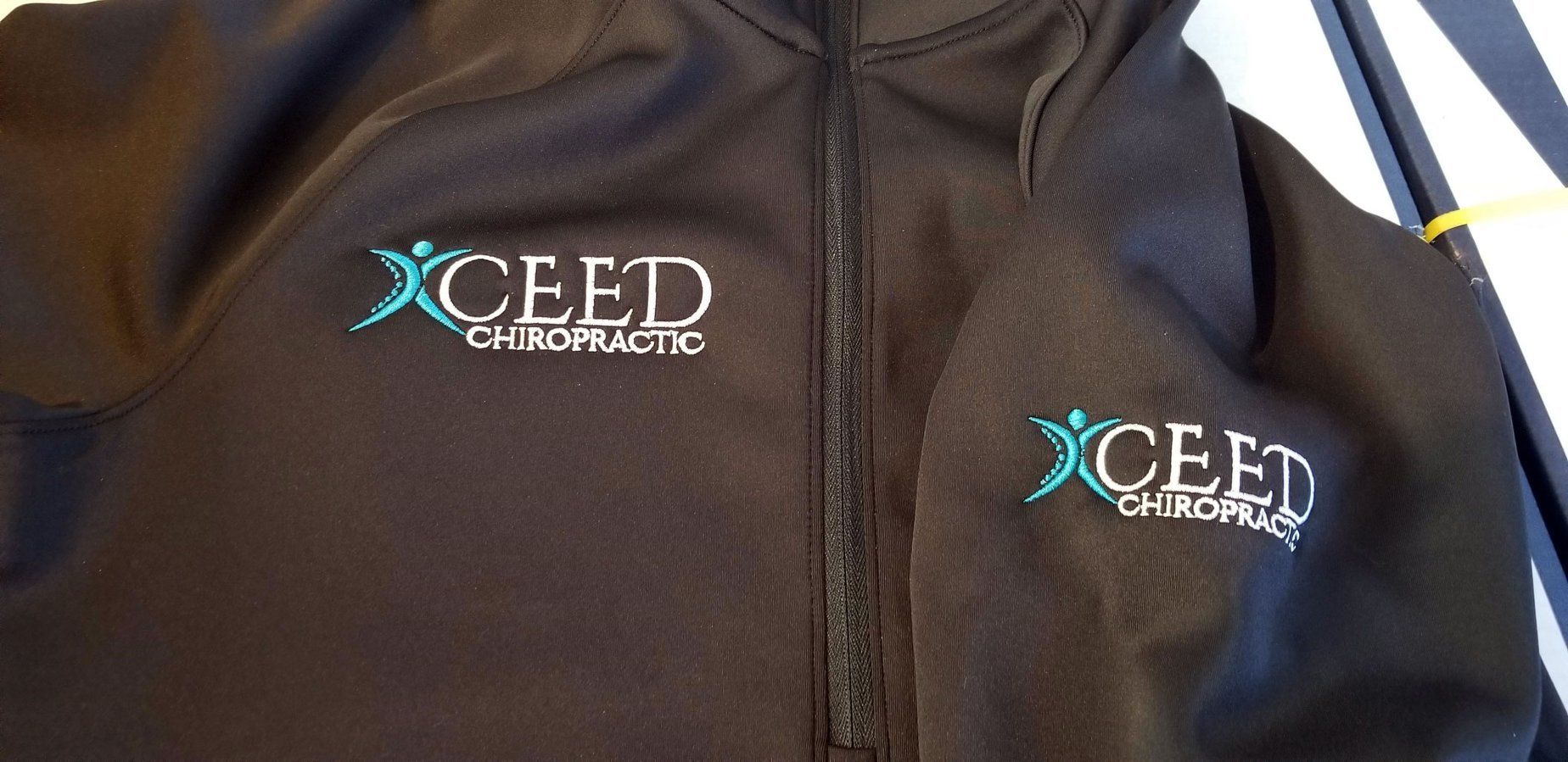 A black jacket with xceed chiropractic embroidered on it