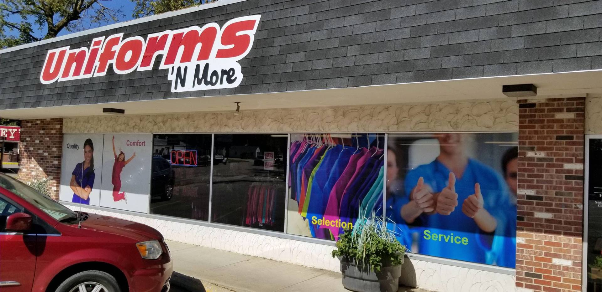 A red car is parked in front of a uniforms n more store.