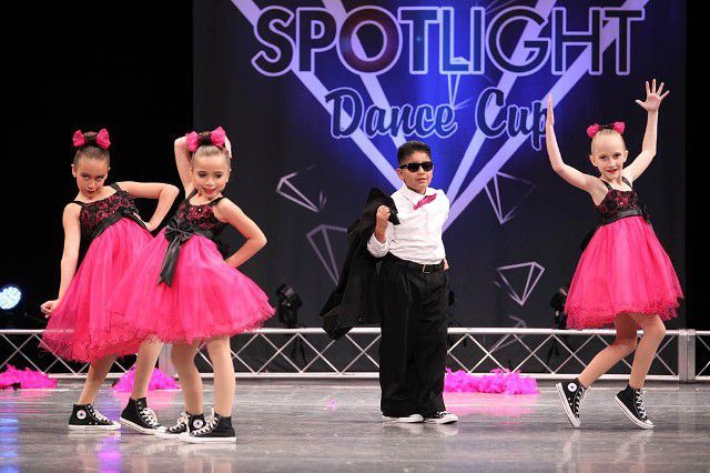 A group of young girls are dancing on a stage in front of a sign that says spotlight dance cup.