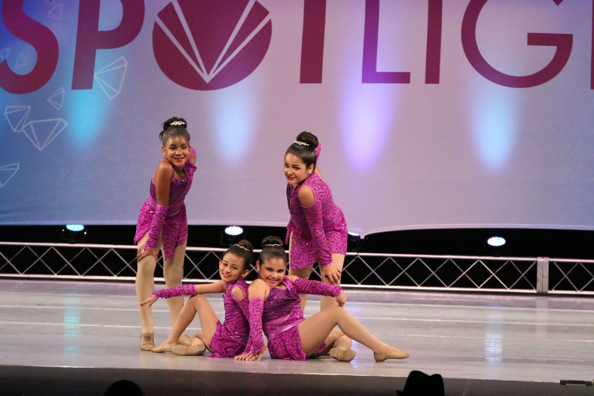 A group of young girls are dancing on a stage in front of a sign that says spotlight.