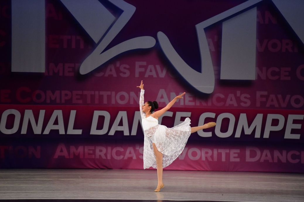 A woman is dancing in front of a sign that says onal dance compe