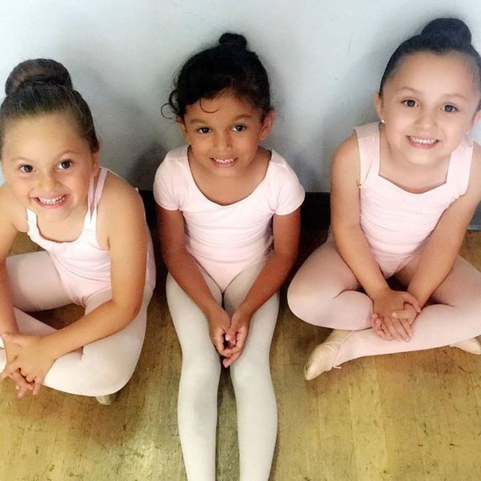 Three little girls in pink leotards are sitting on the floor