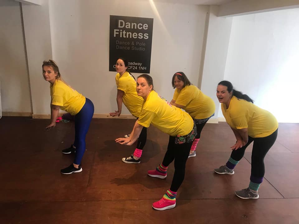 Group enjoying an 80s Fame dance party in Cardiff, wearing colourful retro outfits and leg warmers while learning fun choreography with a professional dance instructor at a Cardiff dance studio.