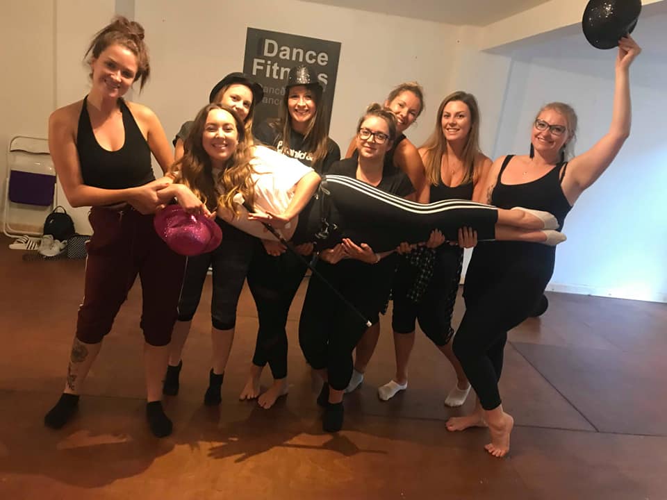 Hen party group wearing “Bride to Be” and “Bride Squad” outfits posing with canes and feather boa in a fun 1920s Charleston dance class