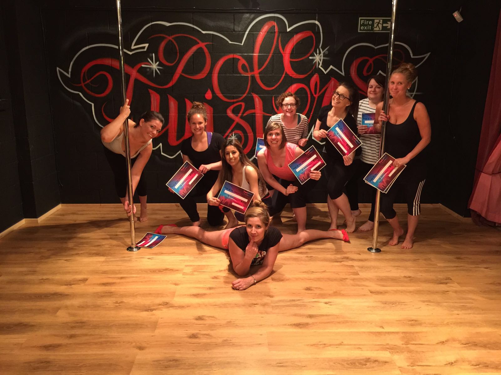 Group celebrating after a pole dancing party in a Cardiff studio, holding certificates and posing together around dance poles