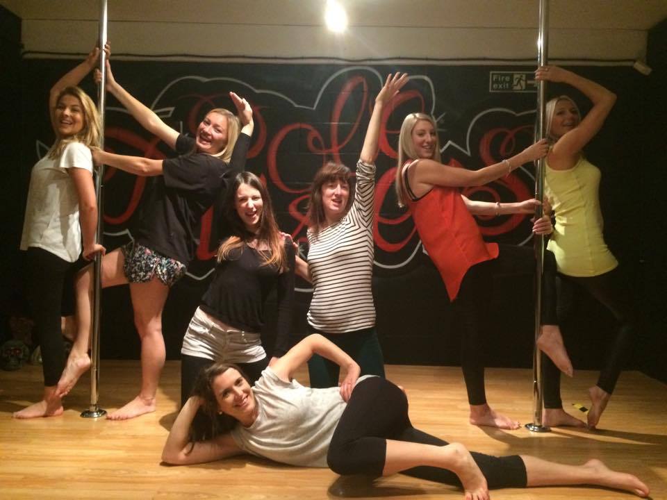 Group of friends posing together during a pole dancing party in a Cardiff studio, smiling and enjoying the experience around dance poles