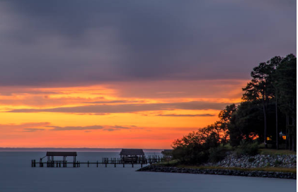 Sunset over water with docks; orange and purple sky; trees on the right.