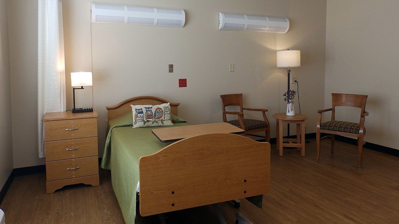A hospital room with a bed , chairs , dresser and lamp