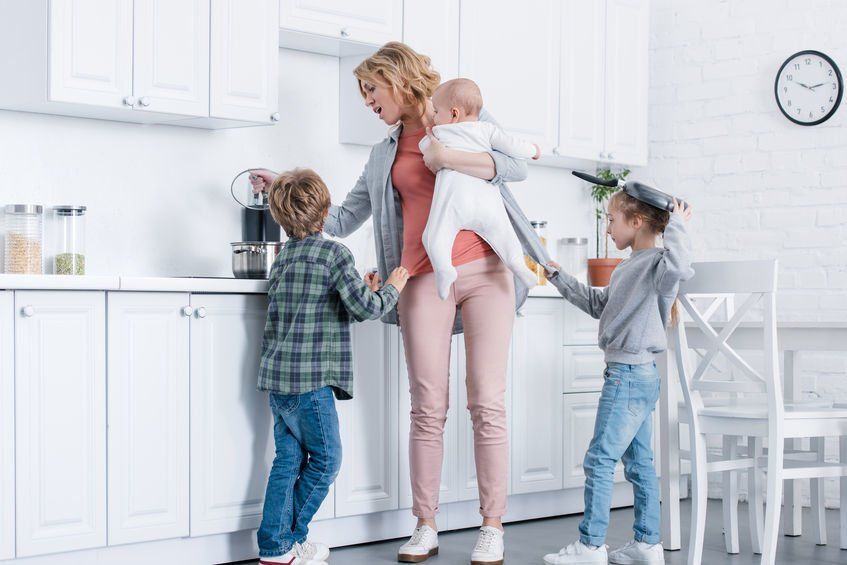 Mom holding a baby while two kids try to get her attention