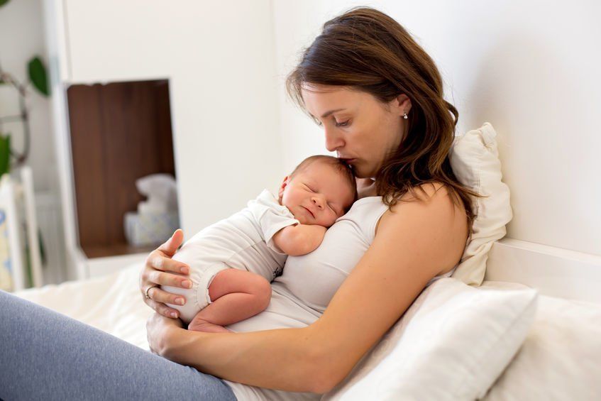 Woman kissing the top of a baby's head while it sleeps