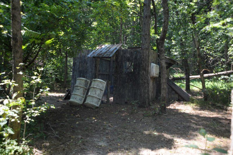 A wooden shed in the middle of a forest surrounded by trees.