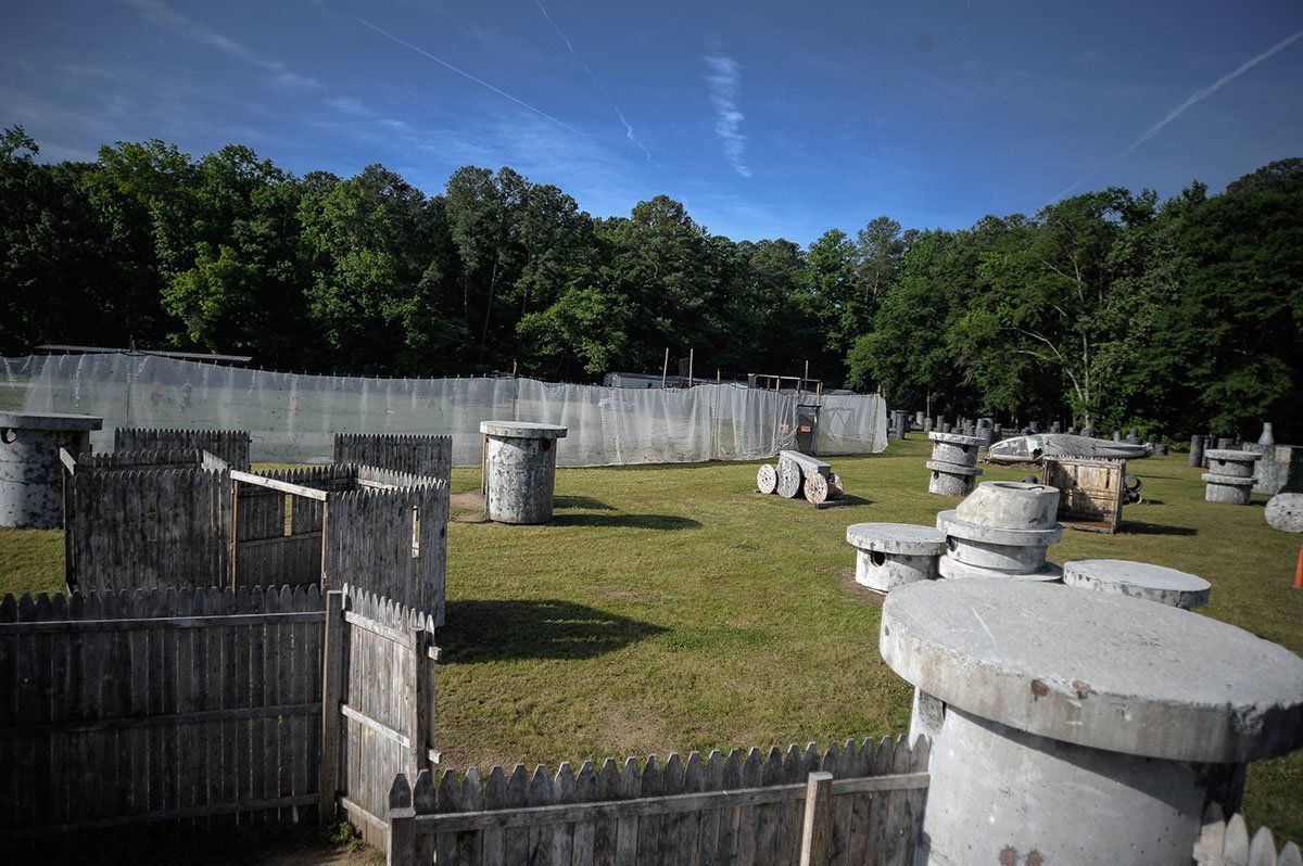 A paintball field with a fence surrounding it and trees in the background.