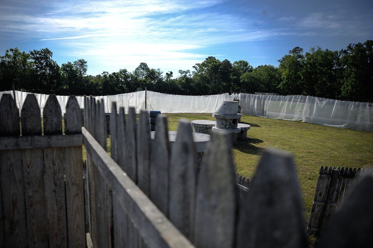 A wooden fence surrounds a grassy field with trees in the background.