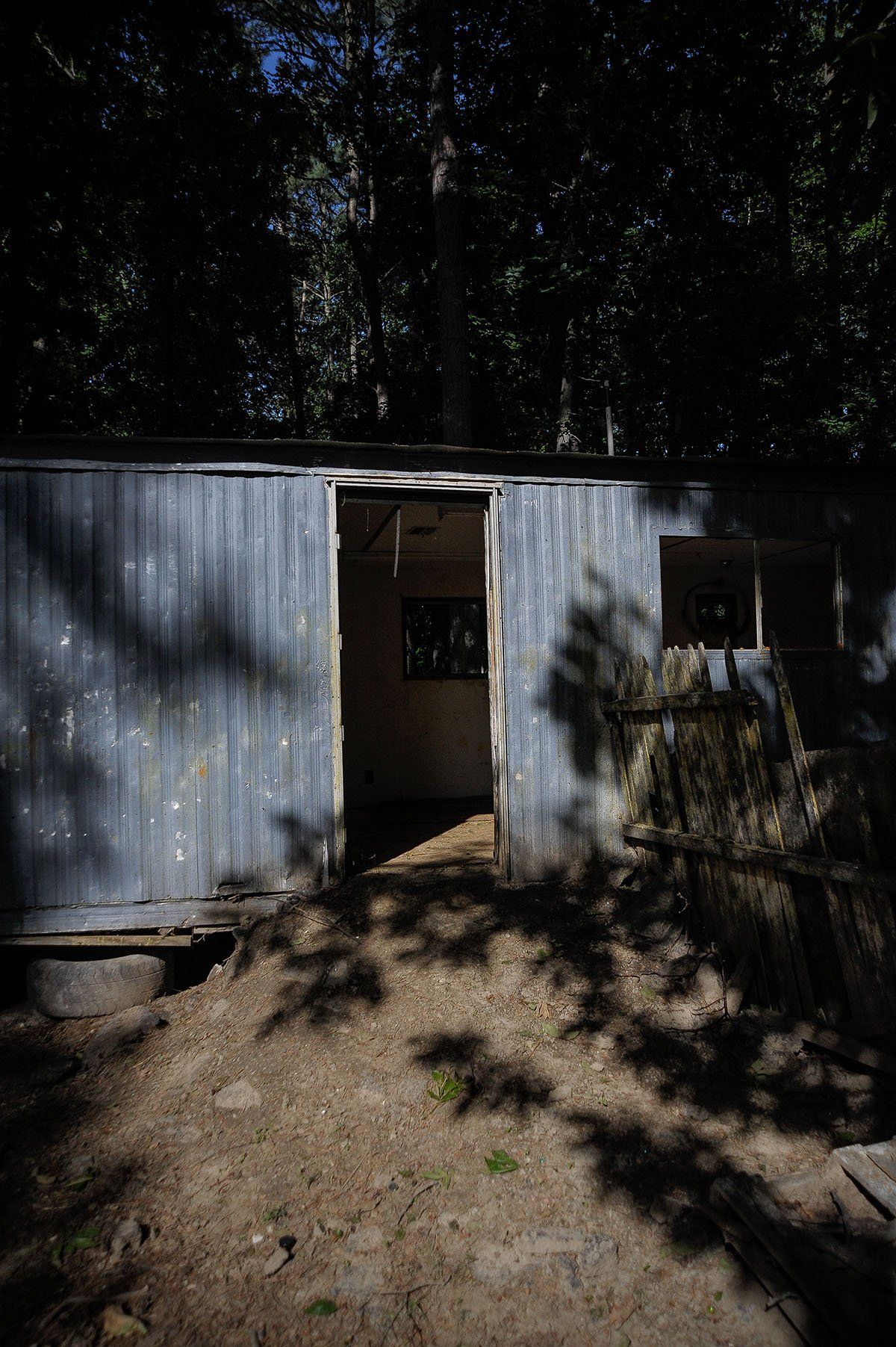 A blue building with a door open in the middle of a forest.
