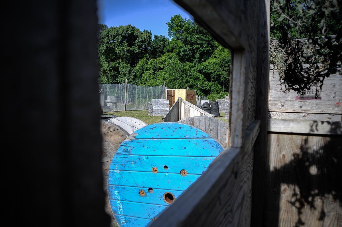 A view of a paintball field through a window with a blue spool in the foreground.