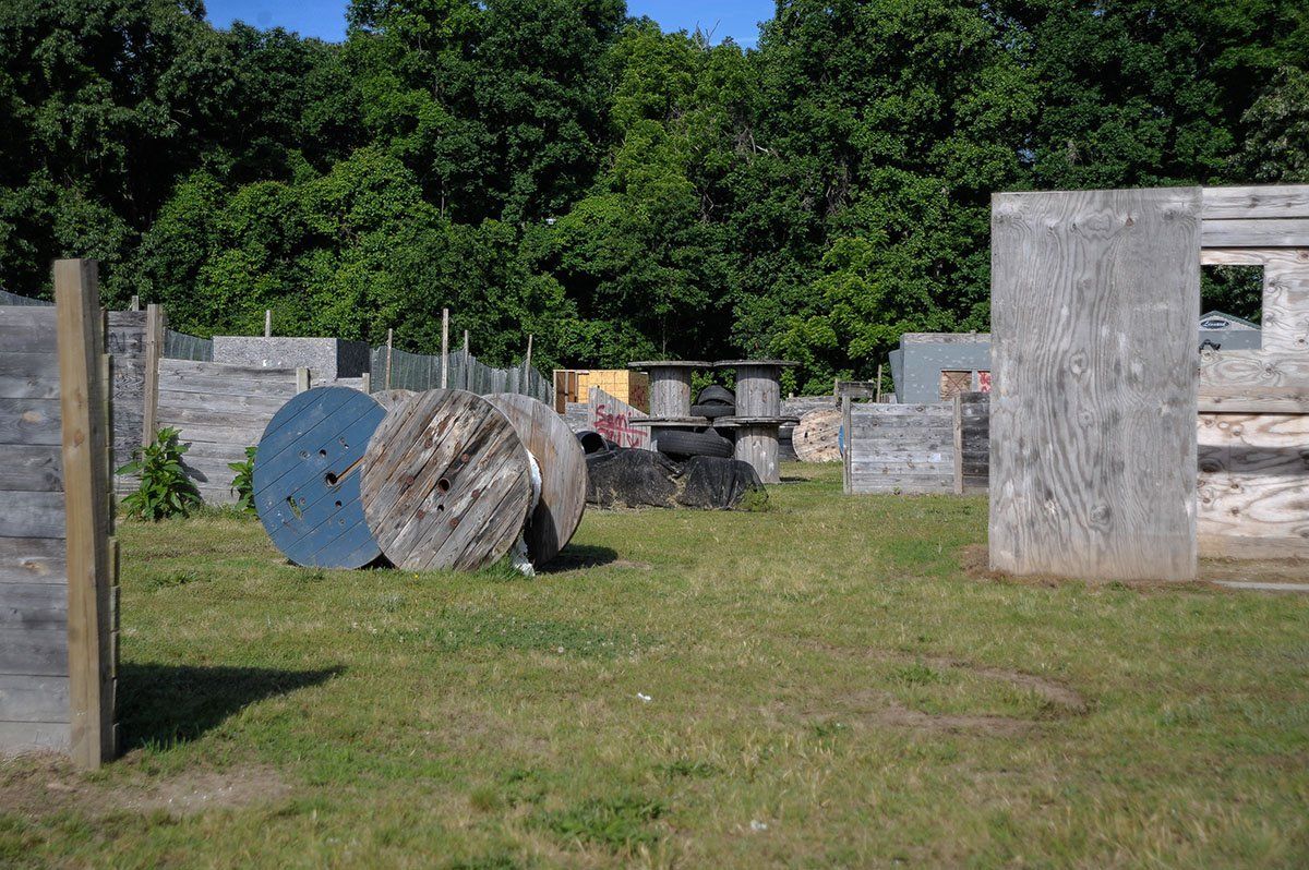 A paintball field with wooden walls and spools in the grass.