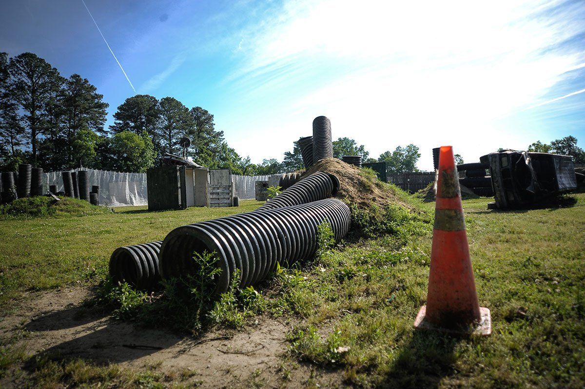 A cone is sitting in the middle of a field next to a pile of pipes.