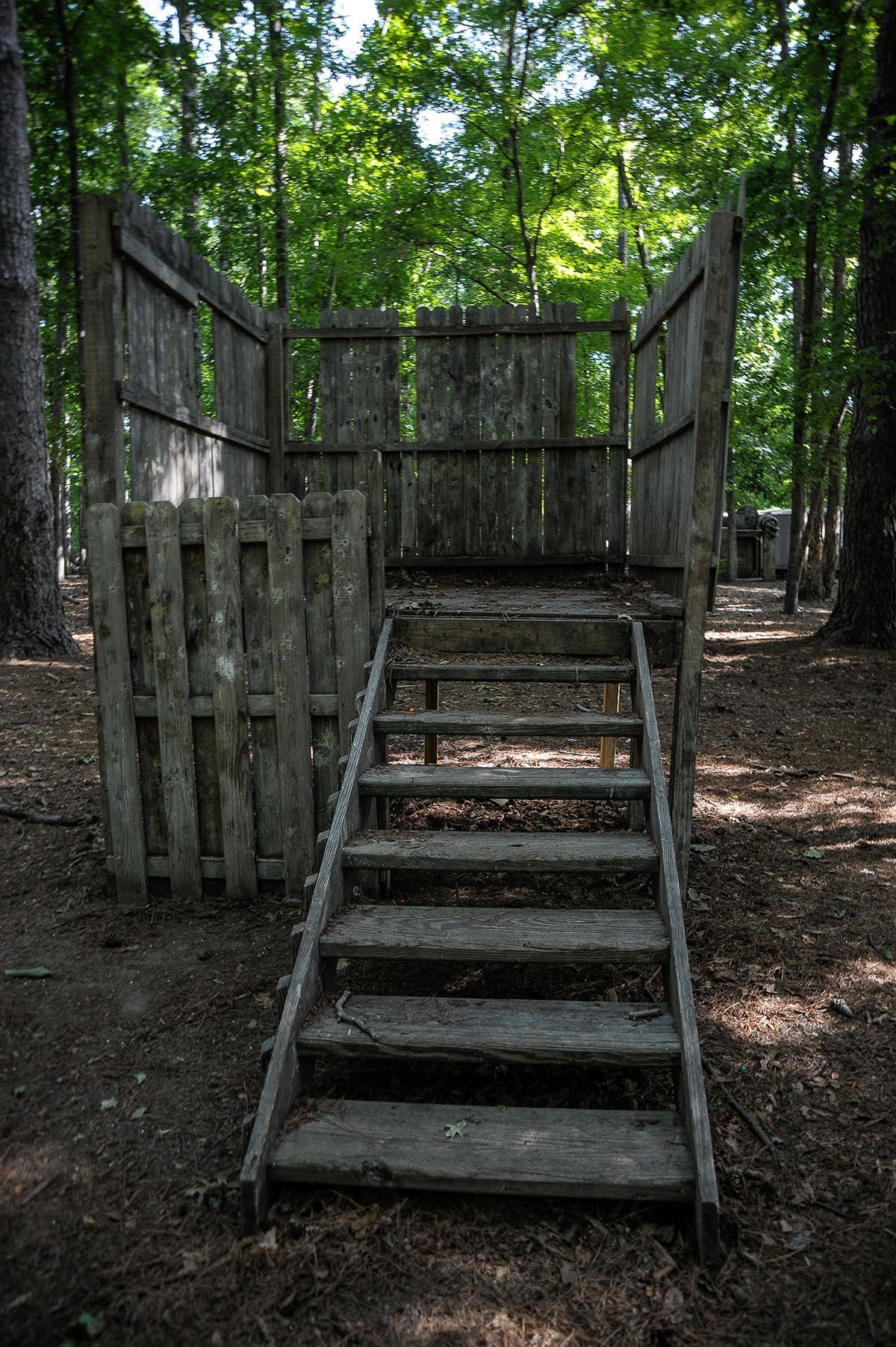 A set of wooden stairs leading up to a wooden fence in the woods.