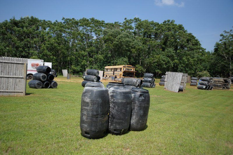 A paintball field with barrels stacked on top of each other and trees in the background.