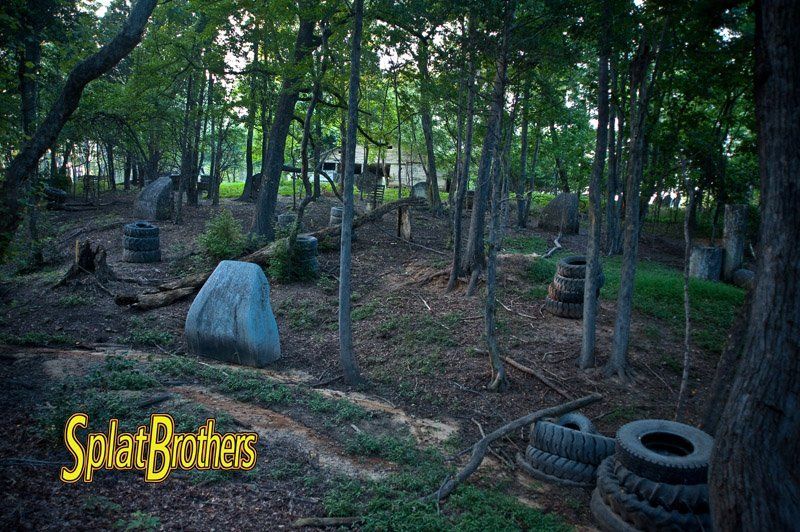 A paintball field in the woods with tires and a large rock.